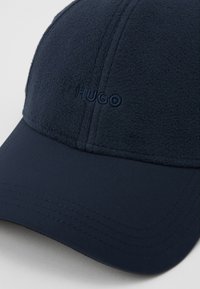 Marineblaue Mütze aus weichem, strukturiertem Stoff mit einem glatten Schirm. "HUGO" in passendem Faden auf der Vorderseite gestickt.