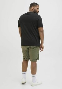 T-shirt noir à manches courtes associé à un short vert olive, avec un ourlet roulé et des baskets blanches. Design simple avec une coupe décontractée.