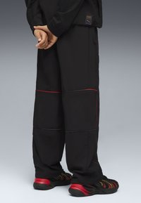 Czarne spodnie sportowe z czerwonymi detalami, w zestawie z czarno-czerwonymi butami sportowymi z paskowanymi akcentami. Teksturowany materiał w luźnym kroju.