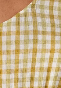 Katoenen stof met een geruit patroon in geel en wit, met een gestructureerde weving en een v-hals ontwerp.