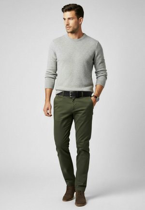 Grauer, strukturierter Pullover, grüne, eng anliegende Hose und braune Schuhe. Der Gürtel ist schwarz. Das Outfit zeichnet sich durch ein einfaches, klassisches Design mit neutralen Farbtönen aus.