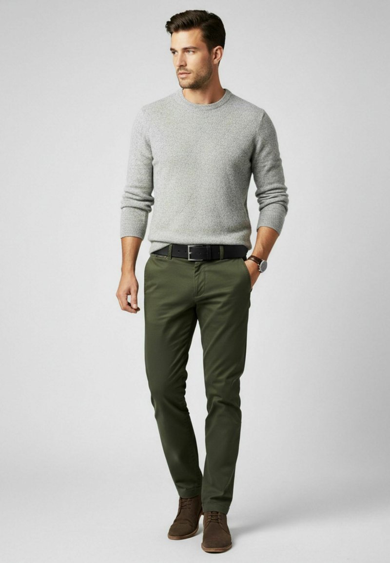 Grauer, strukturierter Pullover, grüne, eng anliegende Hose und braune Schuhe. Der Gürtel ist schwarz. Das Outfit zeichnet sich durch ein einfaches, klassisches Design mit neutralen Farbtönen aus.