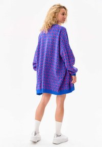 Overgrote gebreide trui in blauw met een geometrisch roze patroon, voorzien van verlaagde schouders en een rechte zoom. Zachte textuur en zijsplitten.