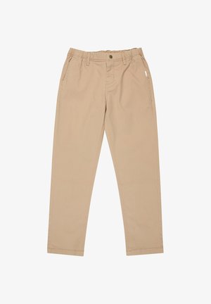 Persona joven que lleva una camiseta negra de manga corta y pantalones beige, de pie con las manos relajadas a los lados, sobre un fondo blanco.