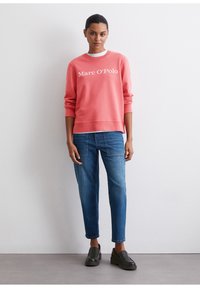Korallivärvi sweatshirt valgete "Marc O'Polo" tekstiga, kombineeritud helesiniste teksade ja mustade platvormsussidega, neutraalses taustas.