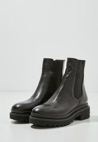 Stivaletti neri in pelle con pannelli elastici laterali, punta tonda e suola in gomma spessa con un motivo a bordi rialzati. Texture liscia.