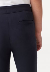 Pantaloni blu navy con una finitura testurizzata, dotati di una discreta tasca posteriore e una vita piatta. Design semplice senza motivi visibili.