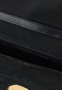 Sort ruskindstaske, der viser en lynlåslomme og et læderremdetalje med synlig syning.