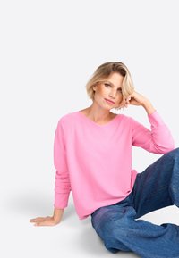 Loose-fitting, long-sleeve, V-neck sweater in bright pink, paired with wide-leg blue denim jeans. Soft texture and relaxed design.