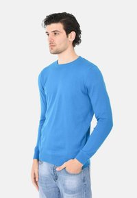 Pullover azzurro a collo rotondo realizzato in tessuto morbido e leggero. Caratterizzato da maniche lunghe e polsini e orlo a coste. Indossato sopra jeans azzurri chiari.