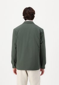Mørkegrønn langermet skjorte med en glatt tekstur, klassisk krage, knappede mansjetter og rett nederkant. Enkel og minimalistisk design.