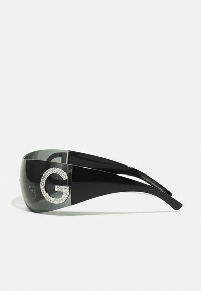 Black sunglasses with a large, mirrored lens, featuring a rhinestone-embellished letter 'G' on the side. Sleek, modern design.