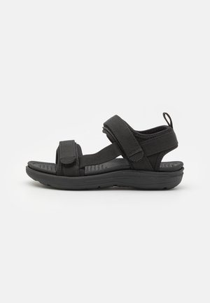 Sort åben-toe sandal med justerbare remme, polstret sål og en trækflig ved hælen, designet til komfort og afslappet brug.