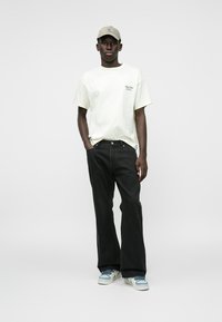 Lichtbeige t-shirt, zwarte wijde jeans en een lichtgrijze pet. Sneakers zijn lichtblauw met witte accenten. Minimalistisch ontwerp, geen patronen.