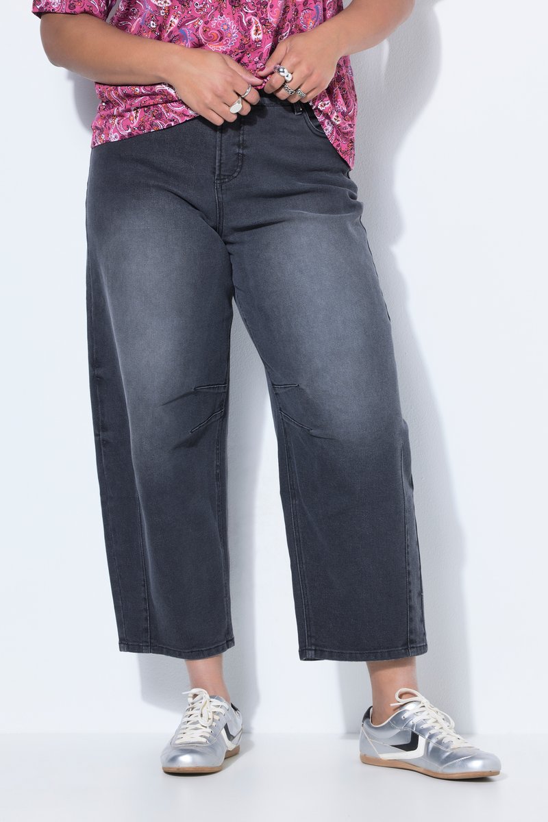 Persona con vaqueros anchos negros recortados, zapatillas plateadas y una camisa rosa con estampado, ajustando el dobladillo de la camisa.