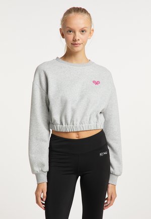 Young woman with blonde hair in a ponytail wears a light grey cropped sweatshirt and black high-waisted leggings with a logo.
