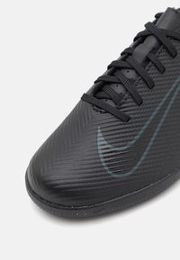 Primer plano de una zapatilla deportiva negra texturizada con cordones negros y un logo de Nike en gris oscuro en el lateral.