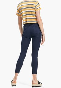 Jeans skinnies en navy y un top corto a rayas amarillas. Los jeans tienen un diseño ajustado y bolsillos traseros. La modelo lleva sandalias de plataforma negras.