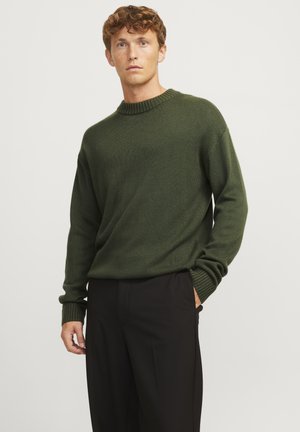 Tume roheline crewneck kampsun ribatud kaela- ja varrukaotstega, veidi lodeva istuvusega, kombineeritud mustade pükstega.