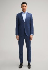 Marineblauer Anzug mit schmaler Passform, Reverskragen und zwei Knöpfen. Hellblaues Hemd mit langen Ärmeln. Schwarze Lederschuhe. Glatte Stoffstruktur.