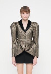 Metallic kuldne ja must jakk suurte puffvarrukatega ja peplum vöökohaga. Omab musta sametist kraed ja kolme nööpi ees.