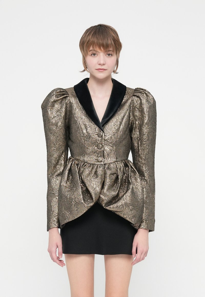 Metallic kuldne ja must jakk suurte puffvarrukatega ja peplum vöökohaga. Omab musta sametist kraed ja kolme nööpi ees.