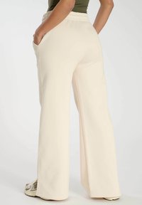 Pantalones de pierna ancha en beige claro, hechos de una tela suave. Cuenta con una cintura elástica y bolsillos laterales. Incluye aberturas en el dobladillo.