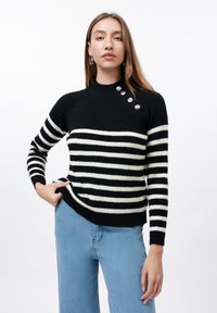 Black and white striped knit sweater with a high neckline and button detail on the shoulder. Features ribbed texture and fitted sleeves.