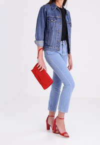 Farkkutakki, musta t-paita, vaaleansiniset farkut, punainen clutch-laukku ja punaiset korkokengät nilkkavöillä. Siistit linjat ja kirkkaat värit.