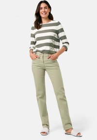 Gestreiftes langärmliges Oberteil in Grün und Weiß mit grafischem Druck, kombiniert mit hellgrünen Hosen und weißen Schlippers.