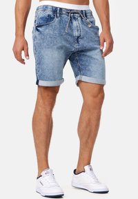 Lichtblauwe denim shorts met een vervaagd effect, voorzien van een trekkoord en omgeslagen manchetten, gecombineerd met witte sneakers.
