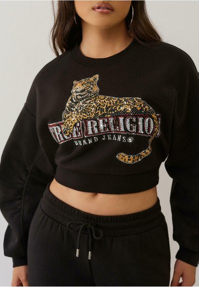 Sweatshirt noir court mettant en avant un graphique de léopard orné de strass. Le design comprend le texte "True Religion" en lettres grasses.