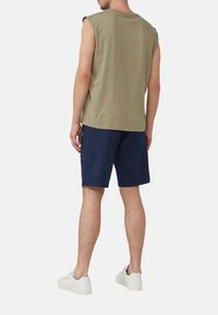 Canotta verde oliva senza maniche con collo tondo, abbinata a pantaloni corti blu navy. L'outfit è completato da sneaker bianche.