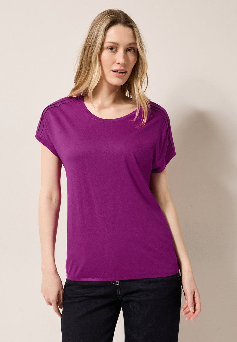 Lila kortärmad T-shirt med rund hals och subtila axeldetaljer. Tillverkad av mjukt tyg, har den en avslappnad passform och slät textur.