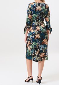 Blumenkleid mit schwarzem Hintergrund; enthält grüne, blaue und orange tropische Muster. Dreiviertelärmel mit Bindeband-Akzenten.