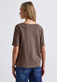 Bruine, kortemouwen t-shirt met een wijde hals en een zachte textuur, gecombineerd met blauwe denim jeans. Eenvoudig ontwerp, geen zichtbare patronen of hardware.
