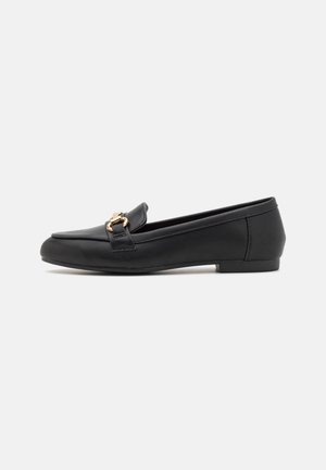 Sort læder flad loafer med guldfarvet metalspænde og lav hæl på hvid baggrund, set fra siden.