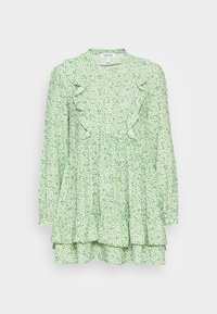 Vestido floral verde com mangas longas, volantes ao longo do corpete, uma cintura franzida e uma saia em camadas com pequenas flores brancas e pretas.