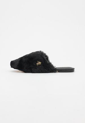 Sandale à semelle plate en fourrure noire, design à bout pointu et accent logo doré. Texture douce sans motifs visibles.
