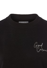Czarny sweatshirt z prążkowanym okrągłym dekoltem, z białym haftowanym napisem "Good Karma" po lewej stronie.