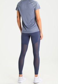 Blå sportleggings med mesh-paneler och reflexdetaljer, tillsammans med en grå kortärmad topp. Materialet verkar lätt och ventilerande.