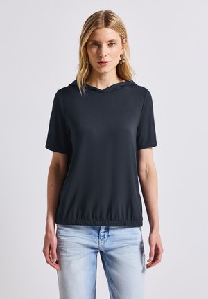 Top negro de manga corta con capucha y dobladillo elástico; tejido suave y ligero; modelo lleva puestos unos jeans de color azul claro.