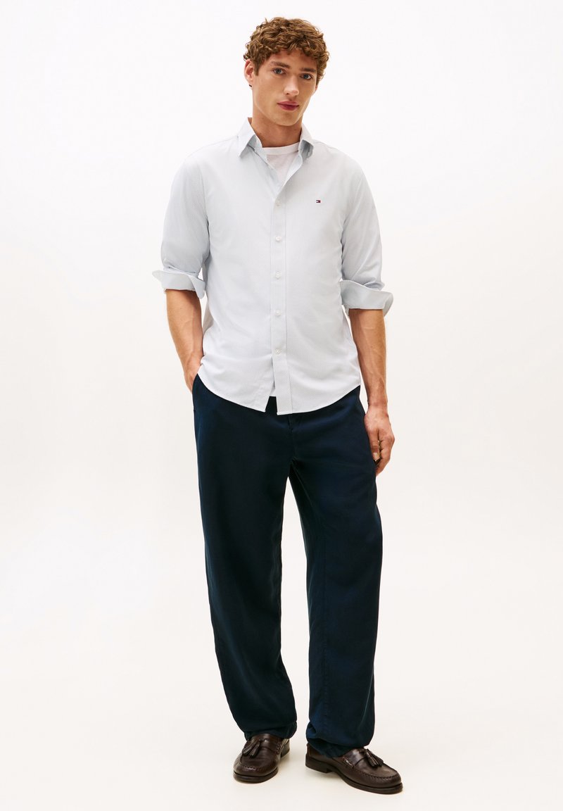 Lichtblauw overhemd met lange mouwen en opgerolde mouwen, marineblauwe broek en bruine loafers. Casual pasvorm, gestructureerde stof, klein logo-detail.