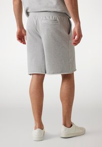 Shorts in cotone grigio con una vestibilità rilassata, dotati di tasche laterali e una tasca posteriore. Il bordo presenta una finitura bianca a contrasto. Indossati con sneakers bianche.