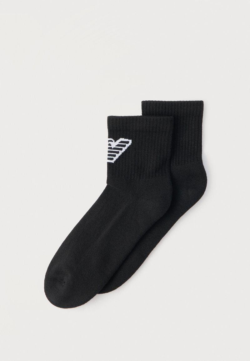 Ζευγάρι μαύρες ριγωτές κάλτσες με λευκό ριγέ λογότυπο κοντά στο πάνω μέρος, εμφανιζόμενες πάνω σε απλό φωτεινό φόντο.