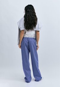 Sweat à capuche gris porté par-dessus un top blanc, associé à un pantalon large à rayures bleues et blanches. La tenue présente une coupe décontractée et des textures douces.