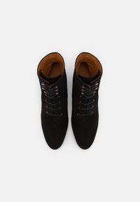 Stivaletti neri in suede con una texture liscia, dotati di punte tonde, sei coppie di occhielli metallici e rivestimento in pelle marrone.
