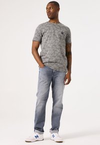 Camiseta gris de manga corta con un patrón de hojas, combinada con jeans azul claro y zapatillas blancas con acentos azules.