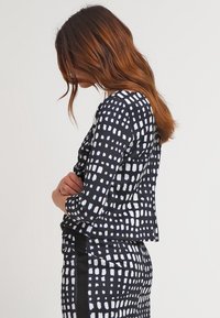 Haut à motifs noir et blanc avec des manches trois-quarts, présentant un motif en quadrillage et une silhouette ajustée. Texture de tissu lisse.