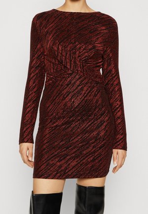 Femme portant une mini-robe à manches longues, ajustée, scintillante avec un motif rouge foncé et noir, col bateau, et des bottes noires montantes jusqu'aux genoux.